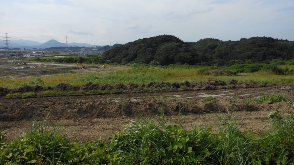 明石台の造成中の区画。手前に土が掘り返された平地が広がり、奥に丘と住宅が見える
