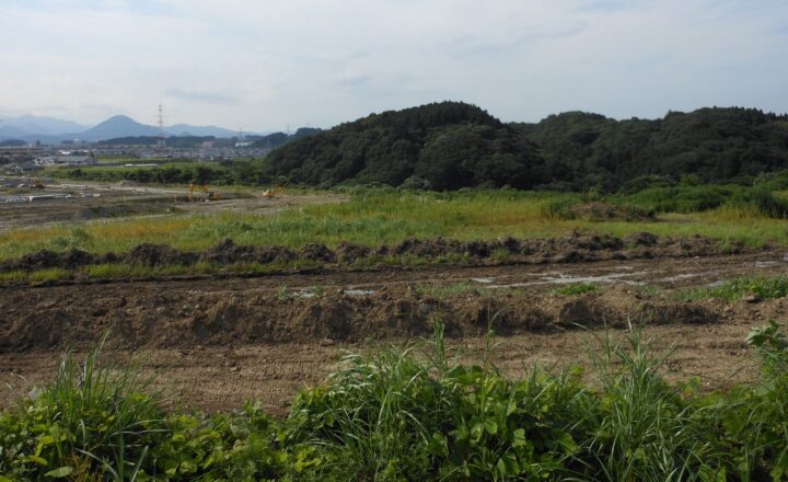 明石台の造成中の区画。手前に土が掘り返された平地が広がり、奥に丘と住宅が見える