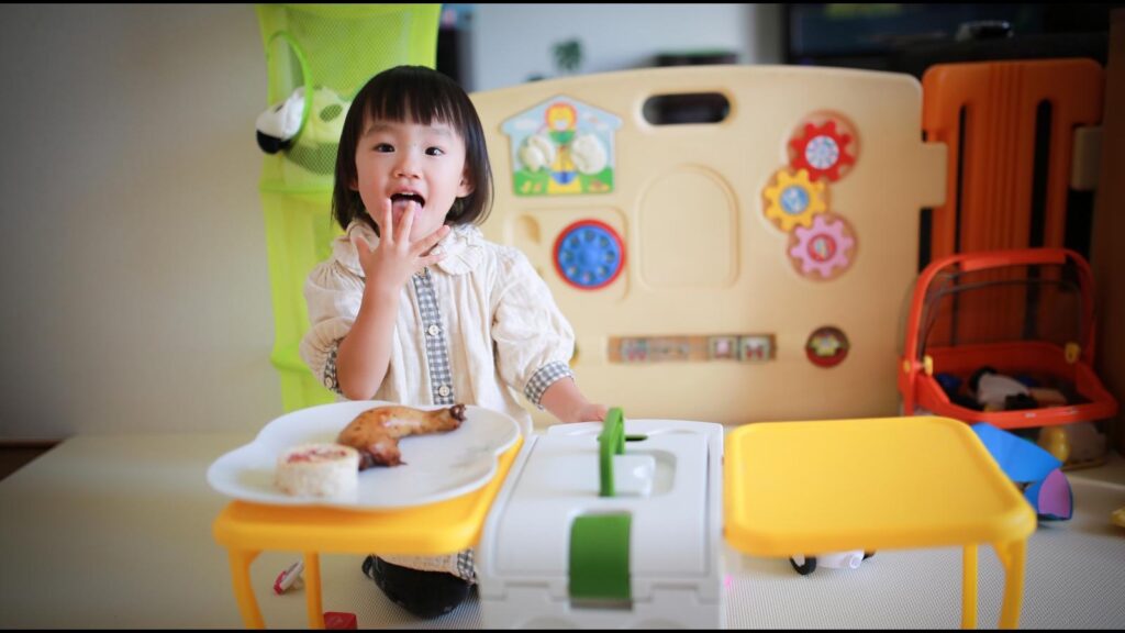 保育室で知育玩具に囲まれておやつを食べる幼い子ども