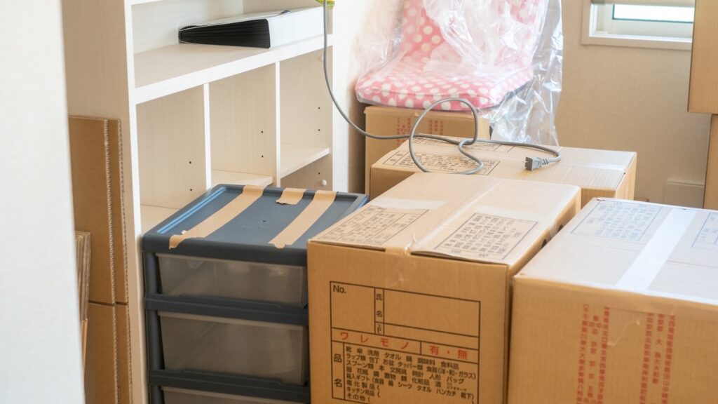 引っ越し前の室内に積み重ねられた段ボール箱と家具