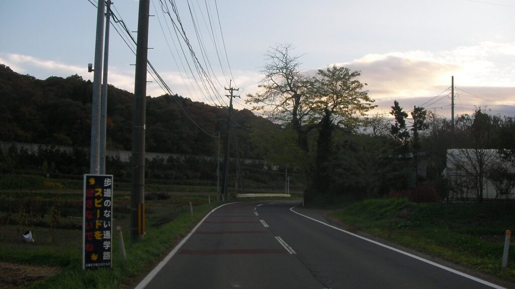 富谷中学校の通学路。夕方の空の下、坂道の両側に電柱と木立が並ぶ