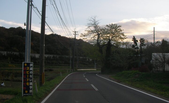 富谷中学校の通学路。夕方の空の下、坂道の両側に電柱と木立が並ぶ