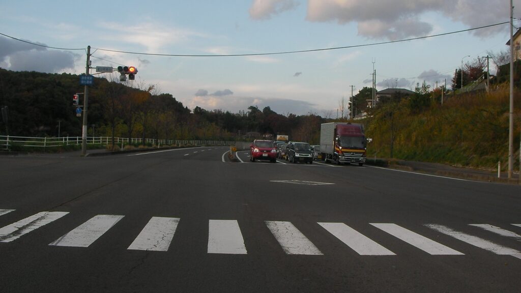 大富団地の入り口の交差点。横断歩道と信号、奥へ続く道路と車列
