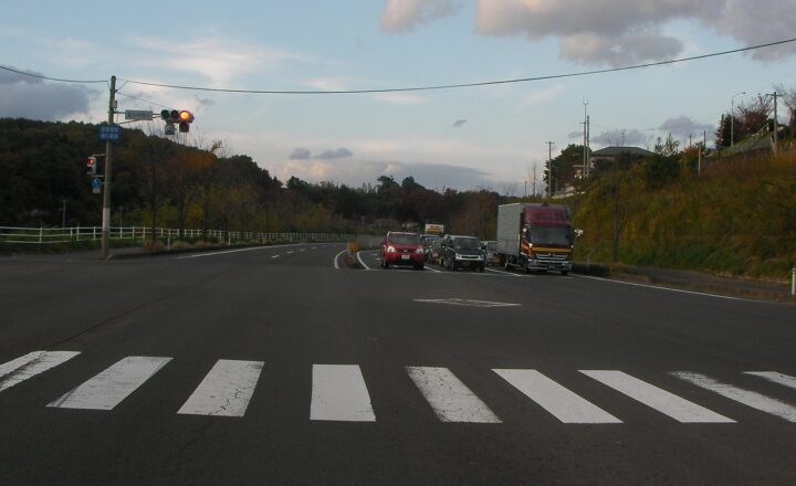 大富団地の入り口の交差点。横断歩道と信号、奥へ続く道路と車列