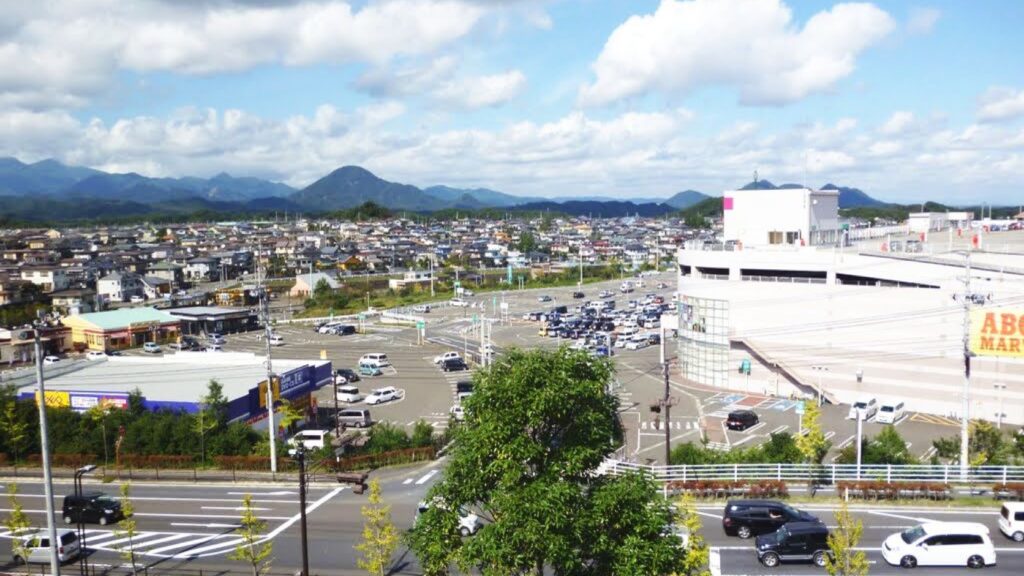 富谷市の市街地を高台から見た風景。住宅地と商業施設が広がり、奥に笹倉山などの山並みが見える