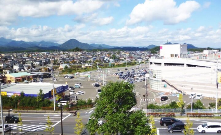 富谷市の市街地を高台から見た風景。住宅地と商業施設が広がり、奥に笹倉山などの山並みが見える