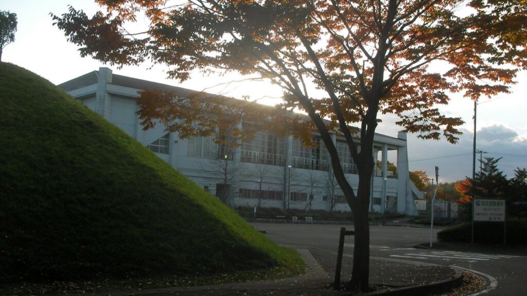 富谷市総合運動公園の体育館。手前に芝の土手と紅葉した木