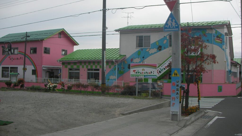 鷹乃杜幼稚園の園舎。ピンクと緑の壁に絵が描かれ、通学路の標識が立つ