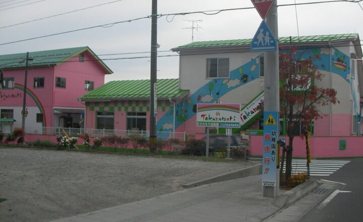 鷹乃杜幼稚園の園舎。ピンクと緑の壁に絵が描かれ、通学路の標識が立つ