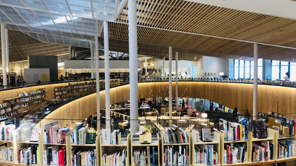 富谷市複合図書館ユートミヤのオープンフロア。曲線を描く木の書架と天井、下階の様子が見える