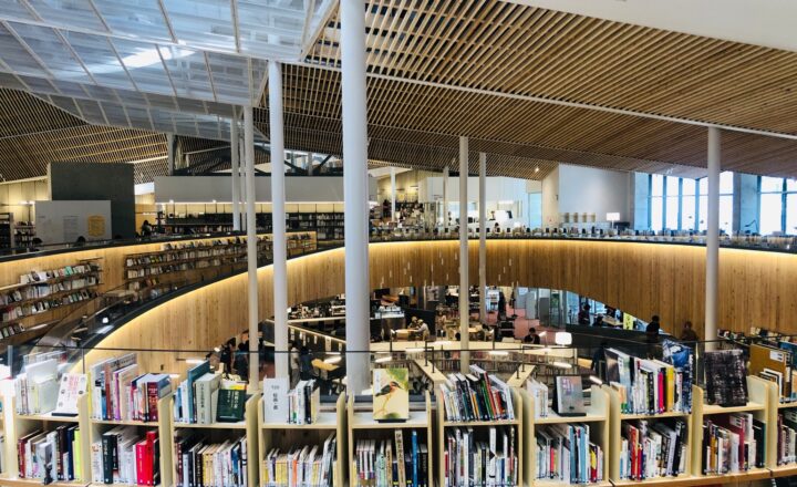 富谷市複合図書館ユートミヤのオープンフロア。曲線を描く木の書架と天井、下階の様子が見える
